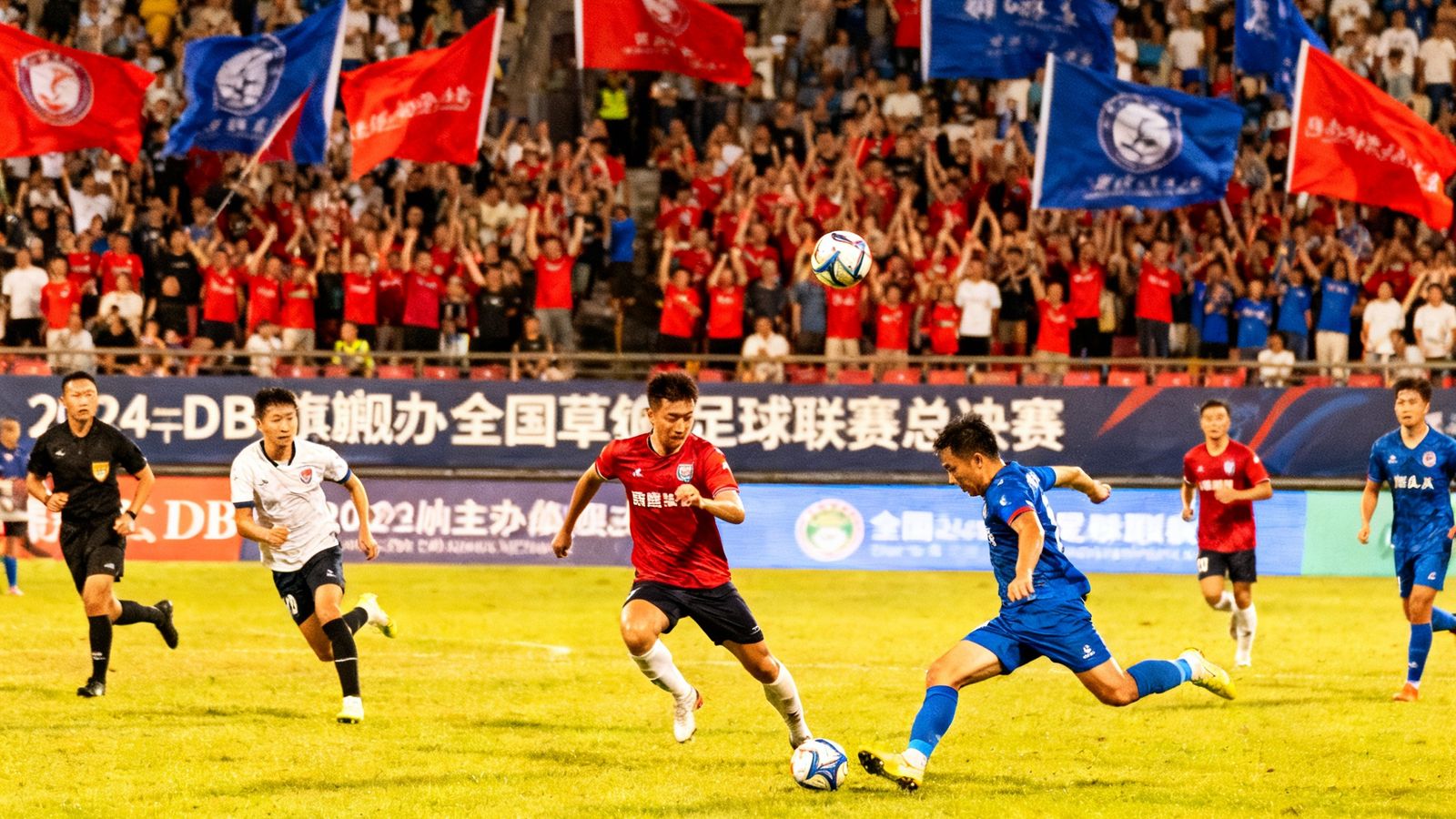 2024年DB旗舰主办的全国草根足球联赛总决赛现场，两支业余球队在绿茵场上激烈拼抢，看台上数千名球迷挥舞旗帜呐喊助威